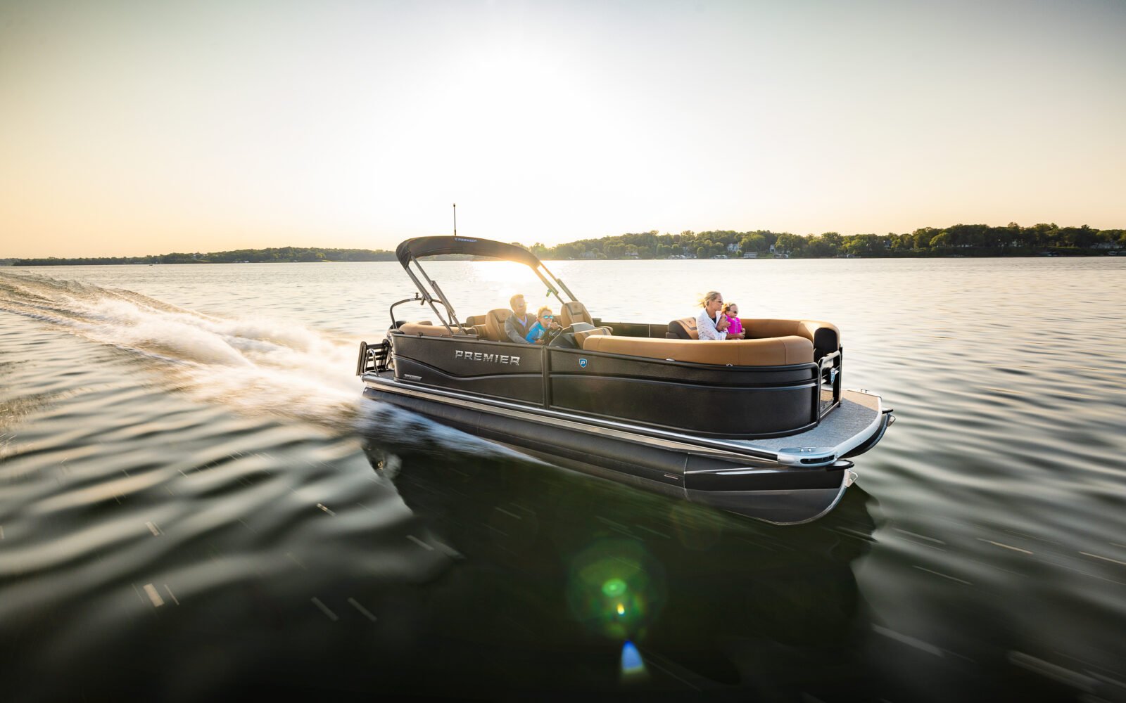 Premier Sunscape pontoon boat cruising across a lake with a family onboard at sunset.