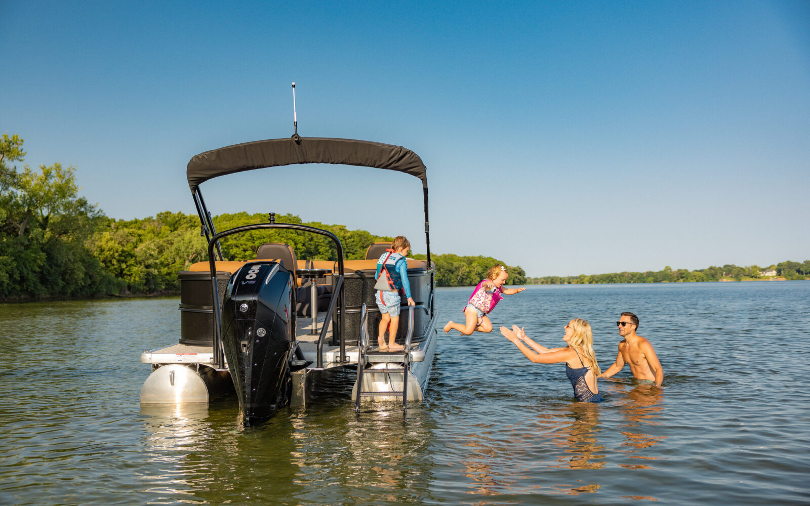 Family swimming and playing behind a Premier Sunscape pontoon boat.