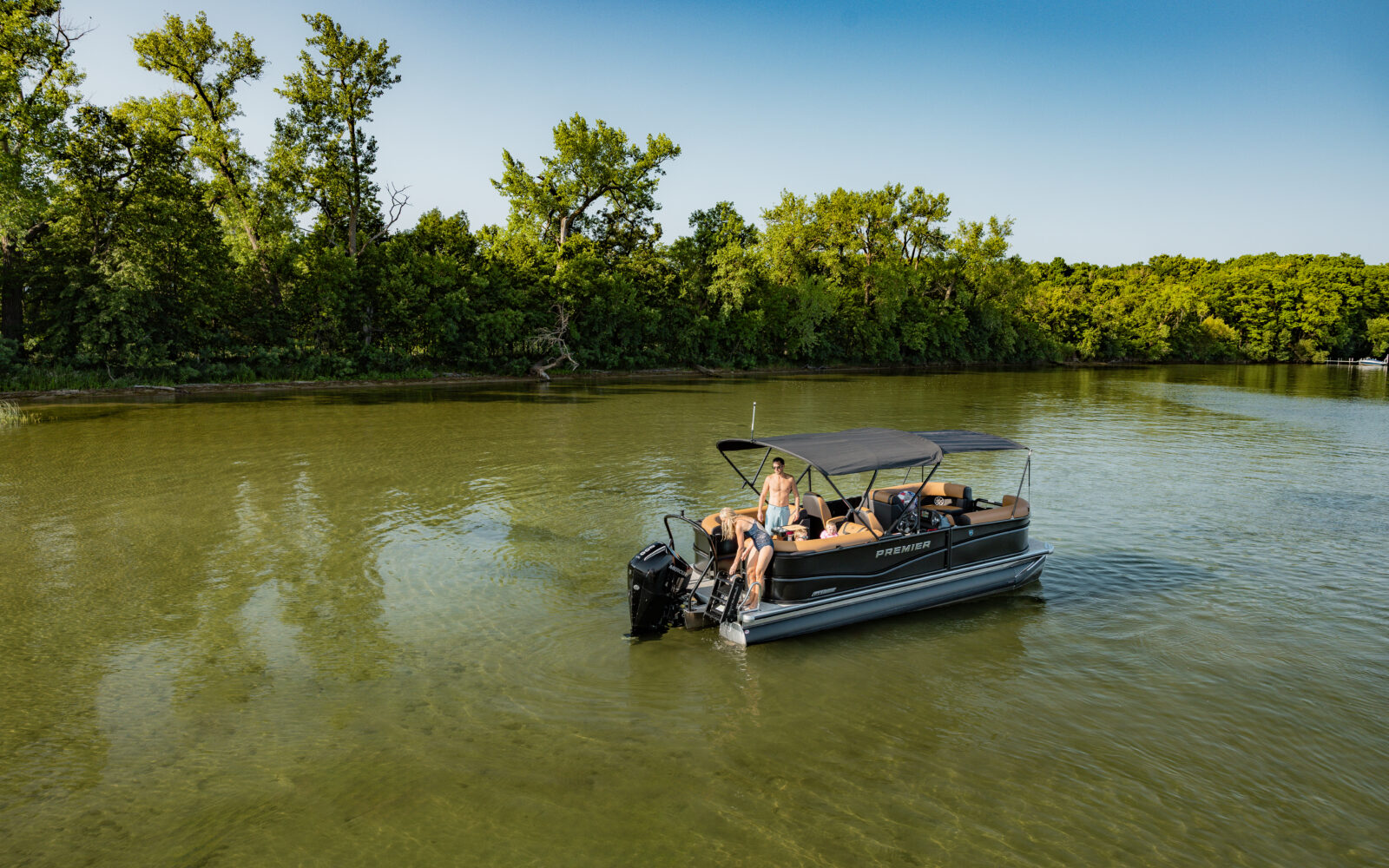 Premier Sunscape pontoon boat anchored in shallow water near shoreline.