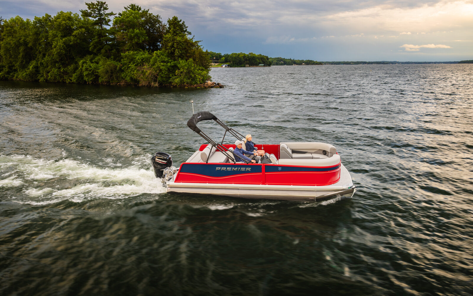 A rear view of the Premier Sunscape pontoon boat showcases spacious stern seating, a Mercury outboard engine, and confident on-water performance while cruising across the lake.