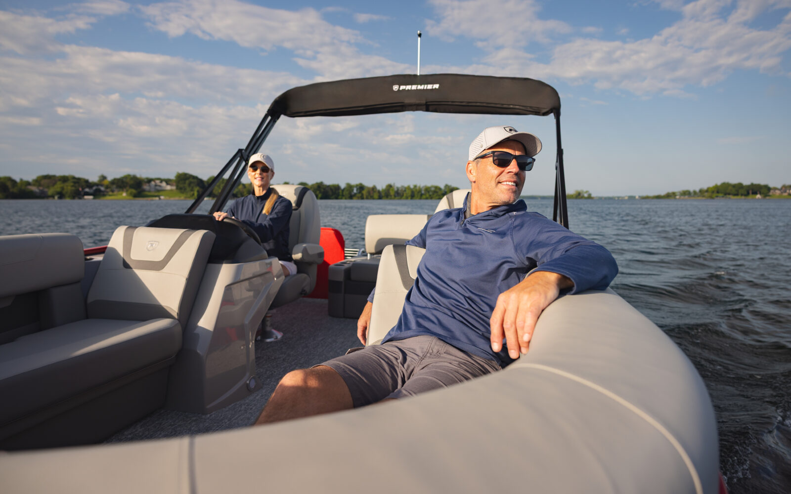 Guests relaxing aboard a Premier Sunscape pontoon boat on a calm lake.